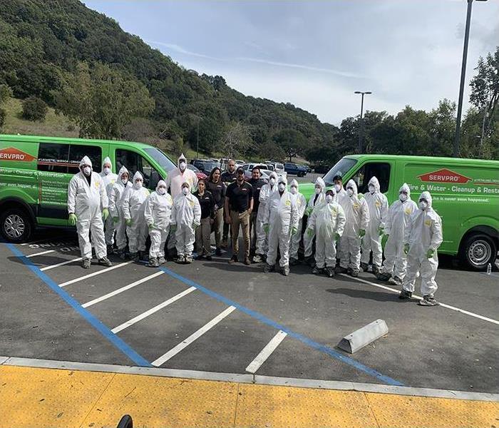 A group photo of SERVPRO professionals in a parking lot with two vans parked on the left and right.